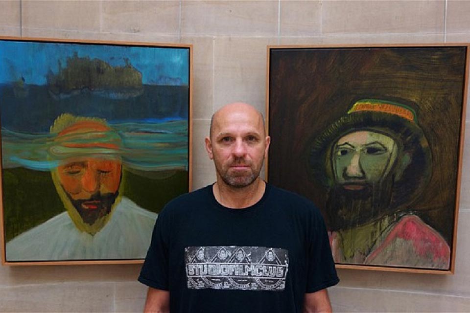 Retrato Peter Doig al lado de pinturas